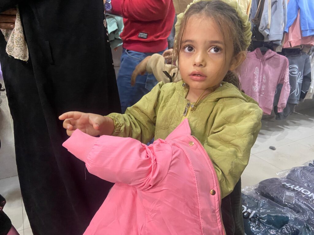 فتاة يتيمة من أطفال غزة تقوم بقياس ملابس شتوية ضمن مبادرة كسوة الأيتام المتضررين من حرب غزة