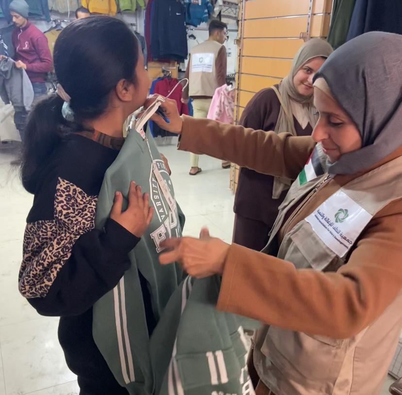 متطوعة من جمعية التحالف للإغاثة والتنمية تساعد طفلة من ذوي الاحتياجات الخاصة في اختيار ملابس شتوية مناسبة في غزة